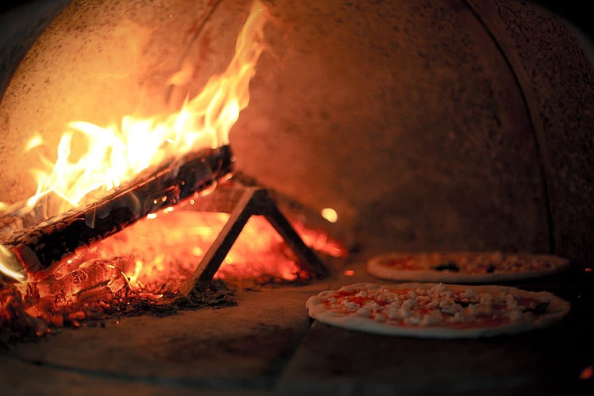 Brennende ved i en pizzaovn, med pizzaer på steinen